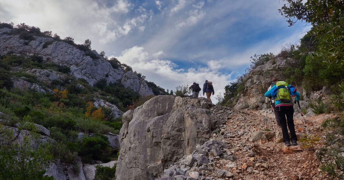 Randonneurs progressant sur un sentier rocailleux entre les crêtes calcaires et la garrigue varoise